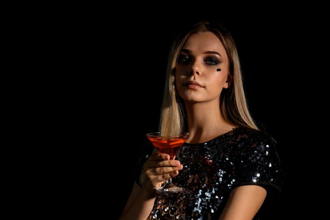 A woman at a party in the style of Halloween with a cocktail in her hands
