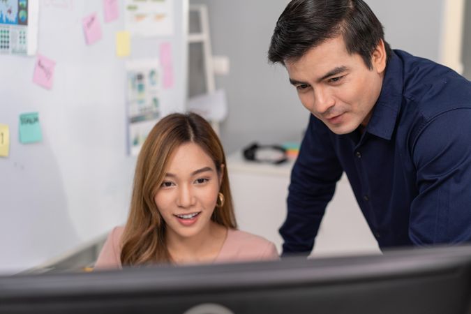 Woman sitting at desk with co worker advising while looking at screen