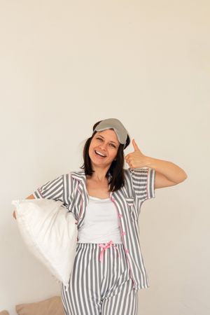 Woman giving thumbs up while holding a pillow, in pajamas.