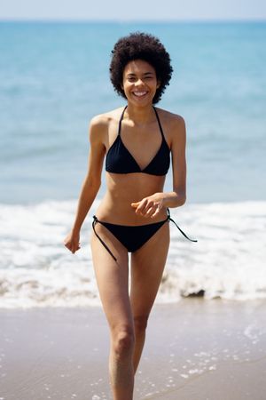 Happy woman walking on shore in bikini