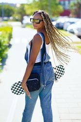 Female in denim overalls standing with skateboard and looking behind her