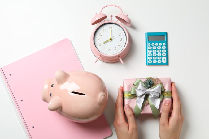 Pig piggy bank, clock and gift box in hands on blank background, top view