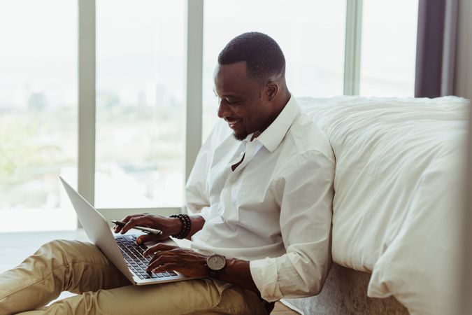 Smiling business man working on laptop from bedroom