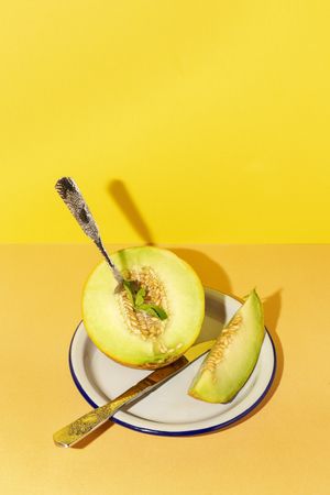 Sliced small melon on plate with spoon and fork
