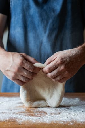 Crop man flattening dough for pizza