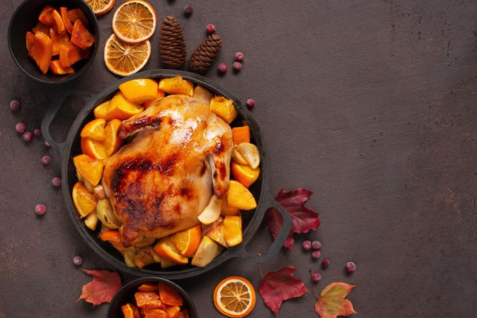 Seasonal table with roasted chicken pot, oranges, autumn leaves and pine cones