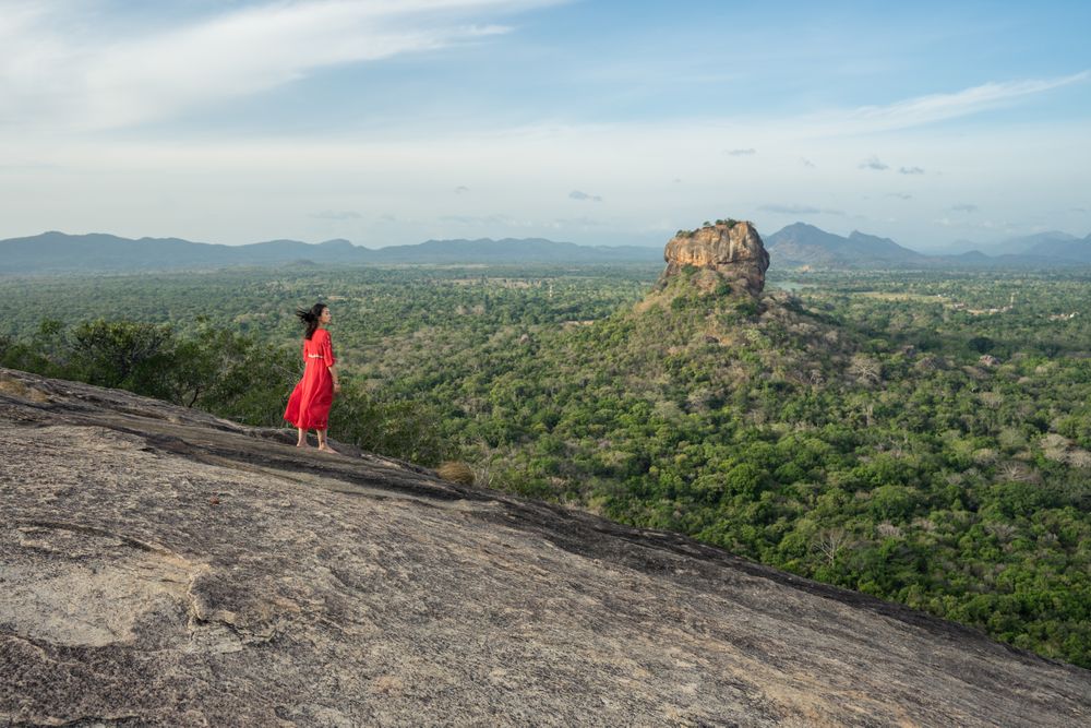 Tourist against solitary rock in middle of green forested plain under clear sky in summer