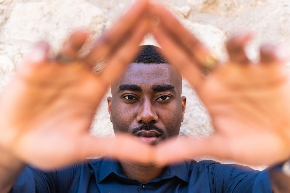Black man showing triangle gesture with hands near wall