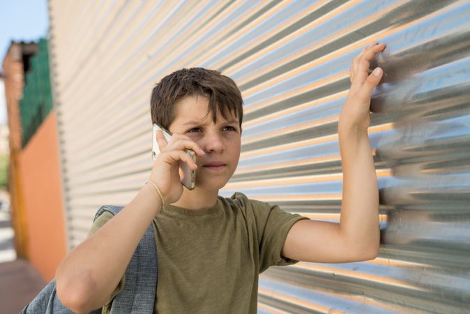 Boy having conversation on smartphone with hand on metal shutter