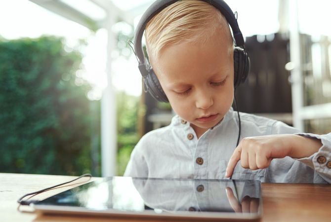 Blond boy using headphones and selecting show or game on digital tablet