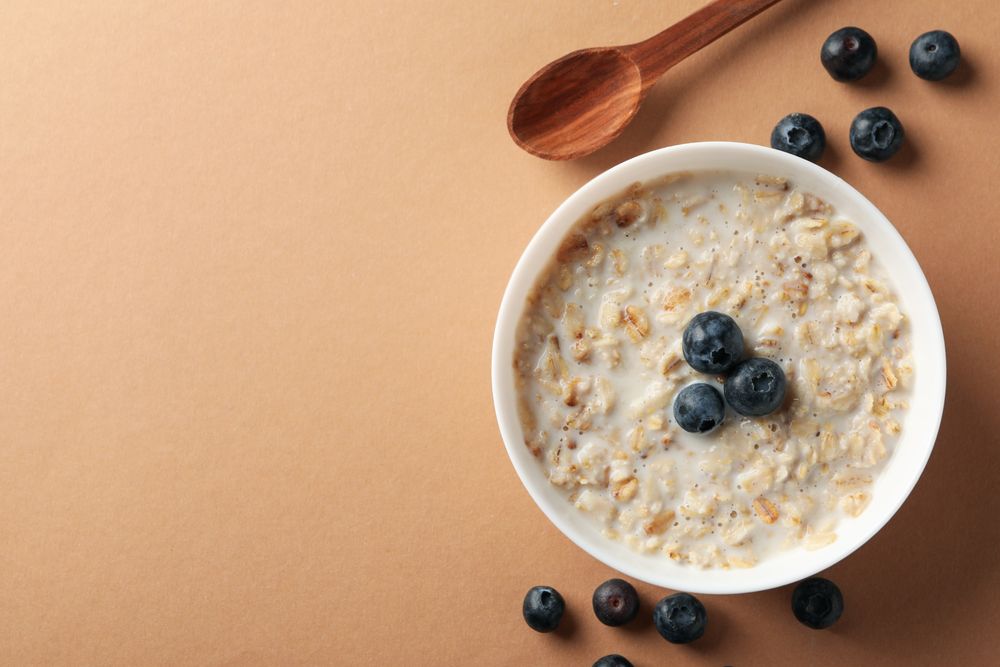Spoon and bowl with oatmeal porridge and berry on craft background