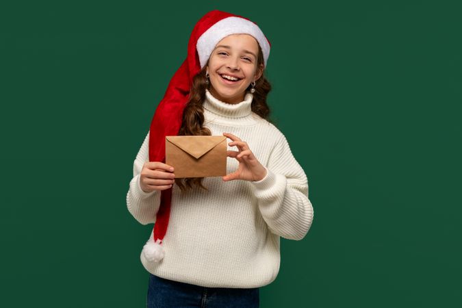 Smiling girl in Santa hat holding brown holiday envelope.