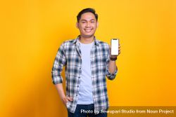 Happy Asian male with hand in pocket and showing blank screen of smart phone 5rejZ0