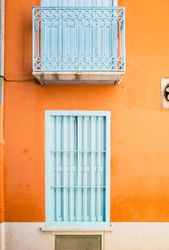 Facade of bright orange wall with baby blue windows and balcony