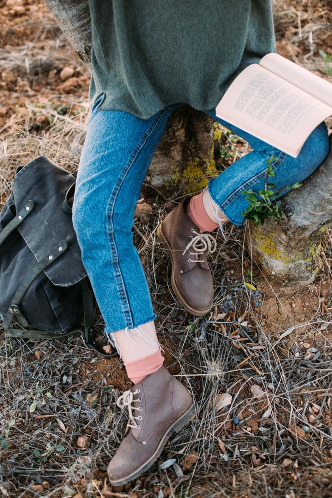 Woman in jeans and boots with book on lap outside