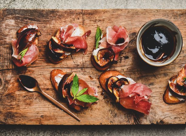 Crostinis with prosciutto, goat cheese and grilled figs on wooden board with balsamic reduction