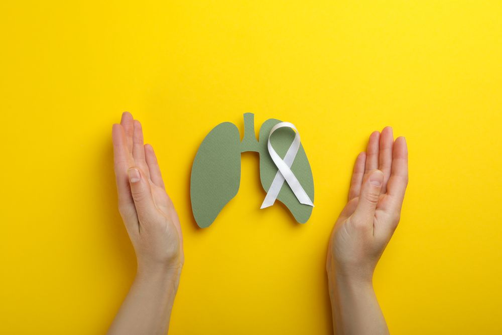 Lungs cut out of green paper with ribbon surrounded by hands