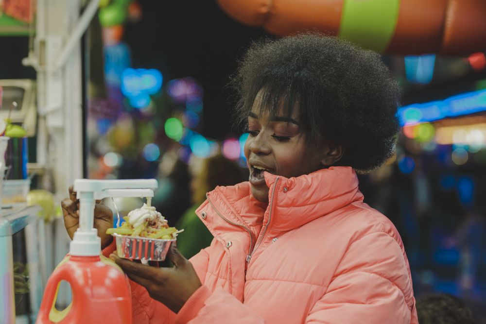 Black woman snacking in amusement park at night