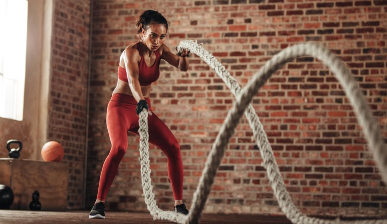 Sportswoman exercising with battling ropes at gym