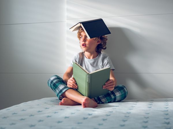 Little boy sitting on bed with books