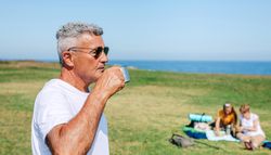 Man enjoying coffee on hike with family sitting in background