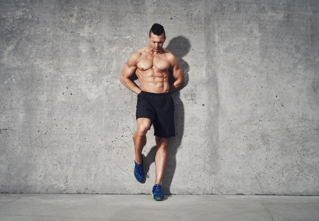 Shirtless muscular man leaning against grey wall