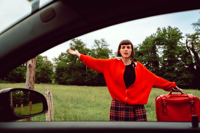 Woman in red sweater gesturing near car on road