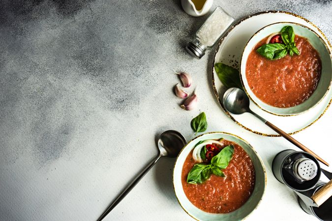 Looking down at two bowls of traditional gazpacho soup with olive oil, basil, garlic and pepper