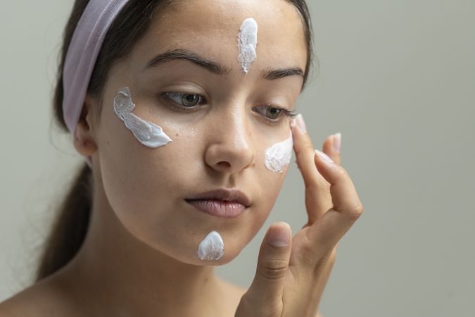 Young woman applying dots of face cream or foundation before blending, skincare routine