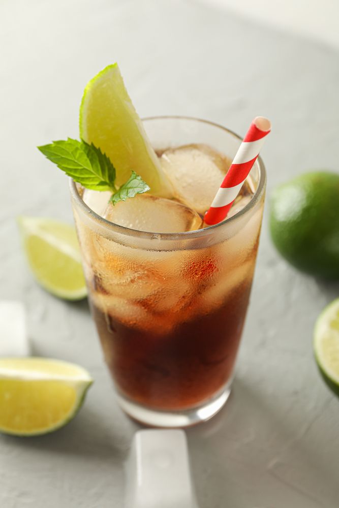 Glass with cold cola and citrus on grey cement background, space for text