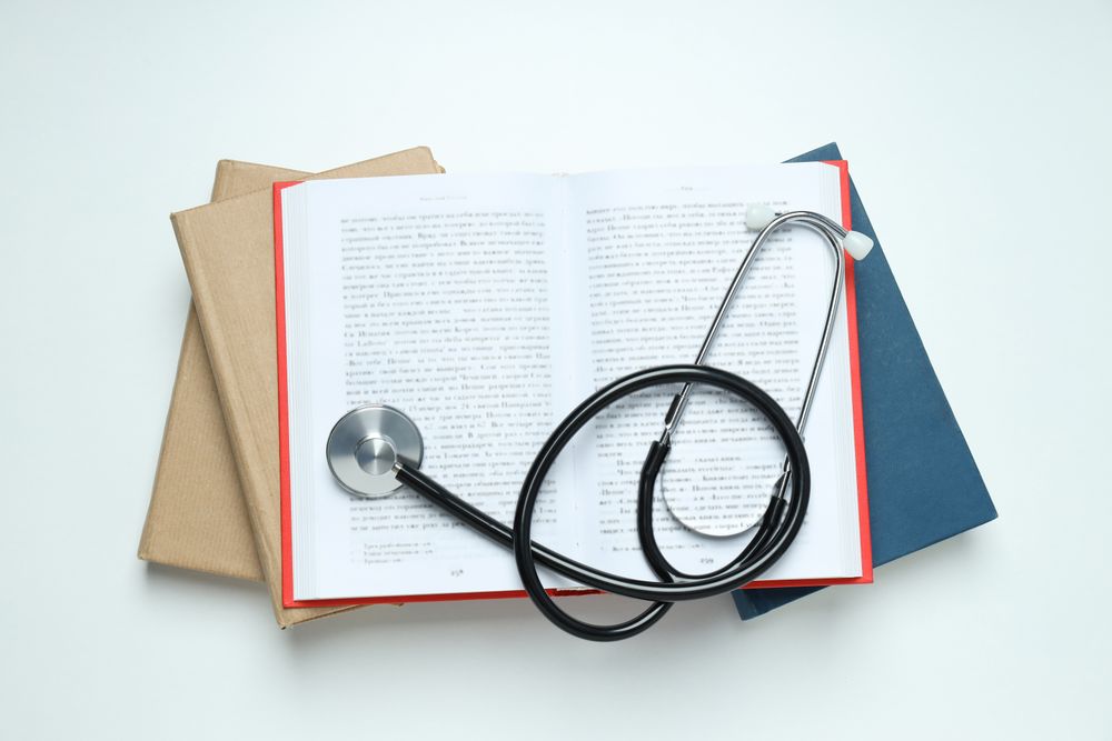 Stethoscope and books on light background, top view