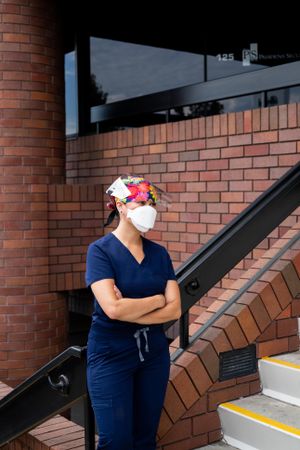 Nurse standing with arms crossed in front of medial building looking away
