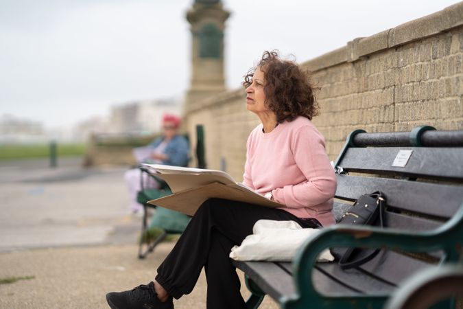 Woman sitting on park bench with drawing board