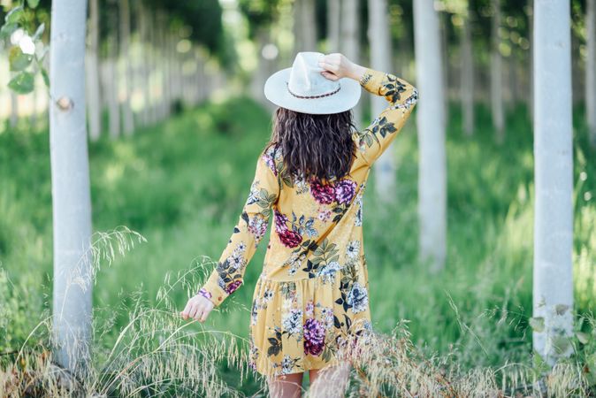 Back of brunette female in yellow dress and straw hat in green field