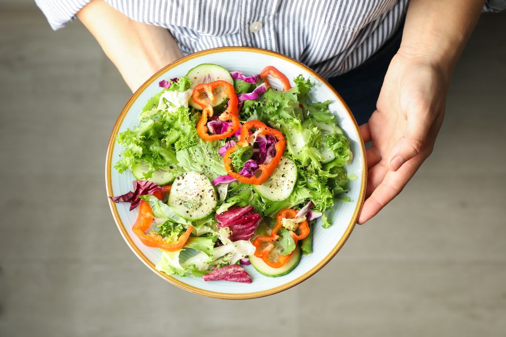 Young woman holding salad on wooden background, top view