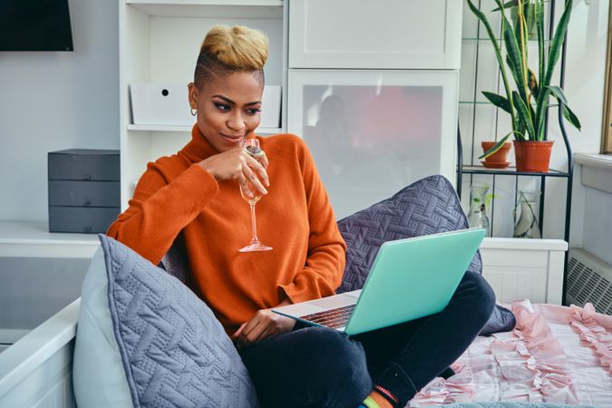 Smiling Black woman sipping champagne while sitting comfortably with laptop