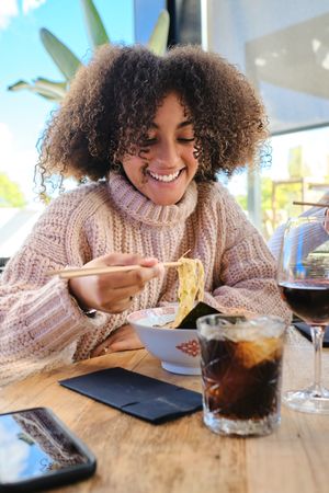Black woman eating noodles in restaurant with toothy smile