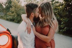Loving couple sitting on car on road near forest