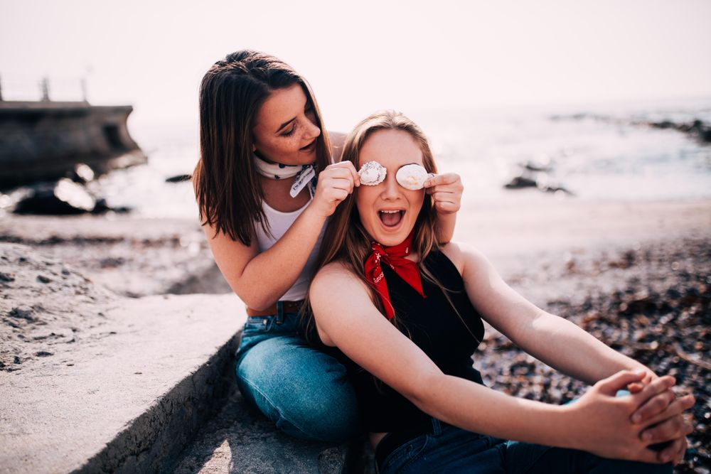 Two young women playing around with seashells on the beach