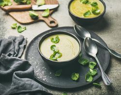 Brussels sprout soup, on dark plate, garnished with fresh sprouts, next to wooden board
