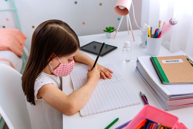 Girl with mask doing homework in her bedroom