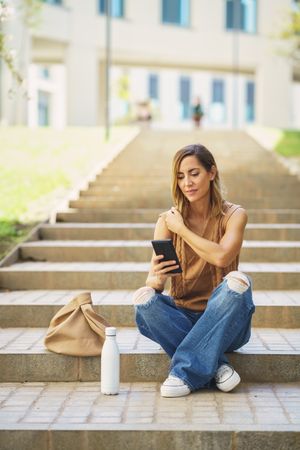 Stylish woman using smartphone sitting on street, vertical