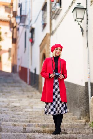 Happy female with camera hanging on neck and looking at camera while standing on aged stone staircase