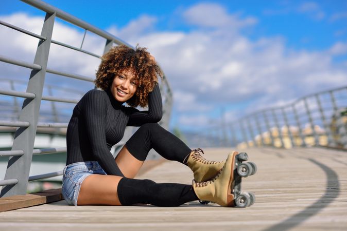 Smiling woman with afro hairstyle posing in roller skates on wooden bridge