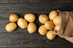 Potatoes pouring onto wooden table from bag
