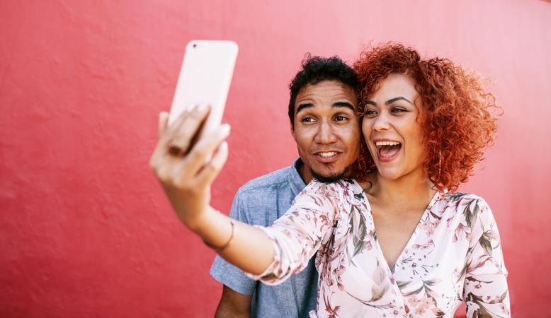 Young woman holding a smartphone for taking selfie with her partner