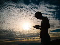 Man with smartphone against cloudy evening sky