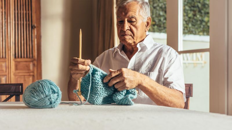 Man knitting warm clothes with wool yarn on table