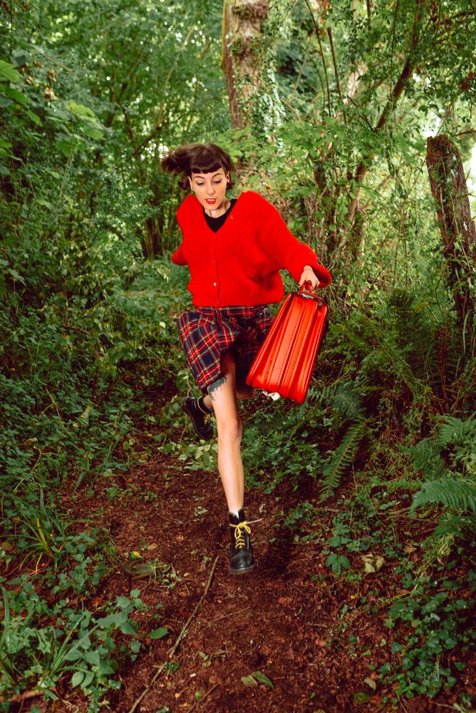 Woman in red with big red suitcase in forest
