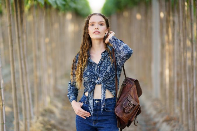A Confident Young Woman Dressed in Trendy Denim with a Stylish Backpack in a Serene Nature Setting